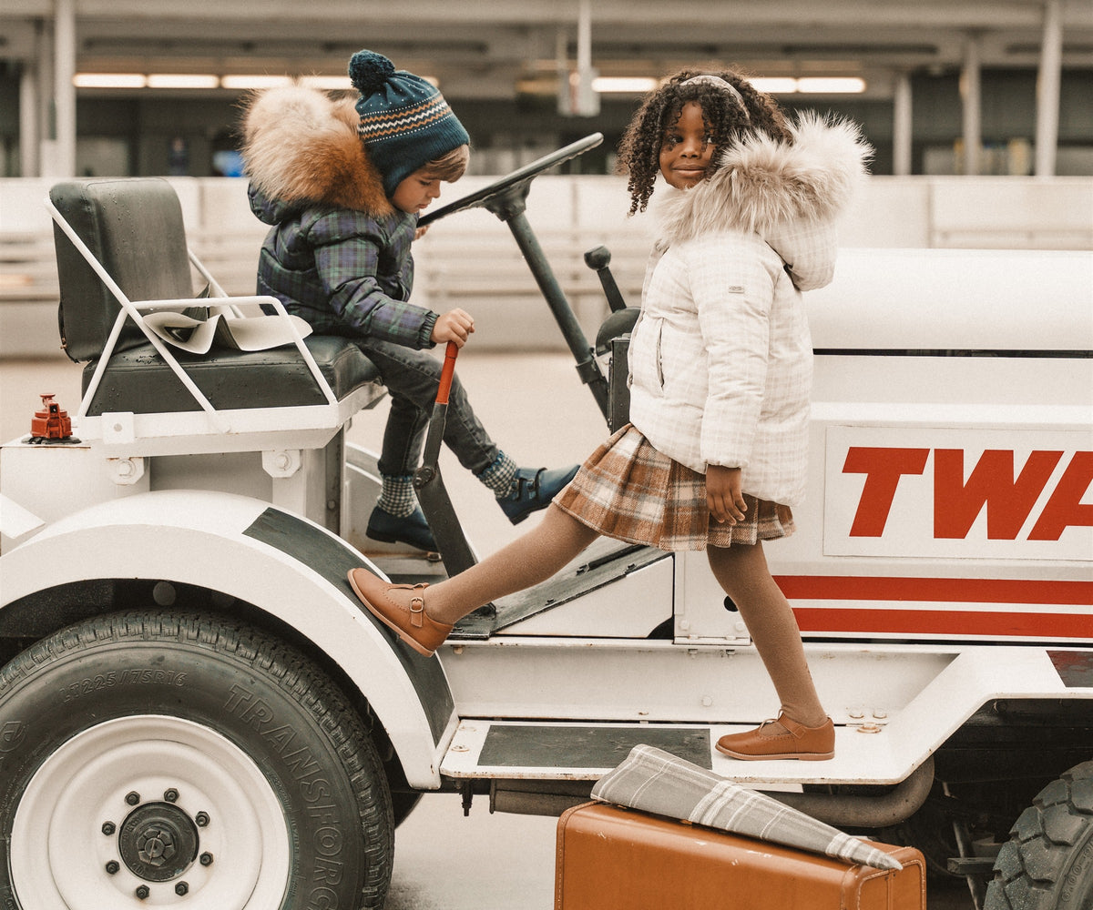 Two children in winter coats playing on a TWA airport tractor with a vintage suitcase